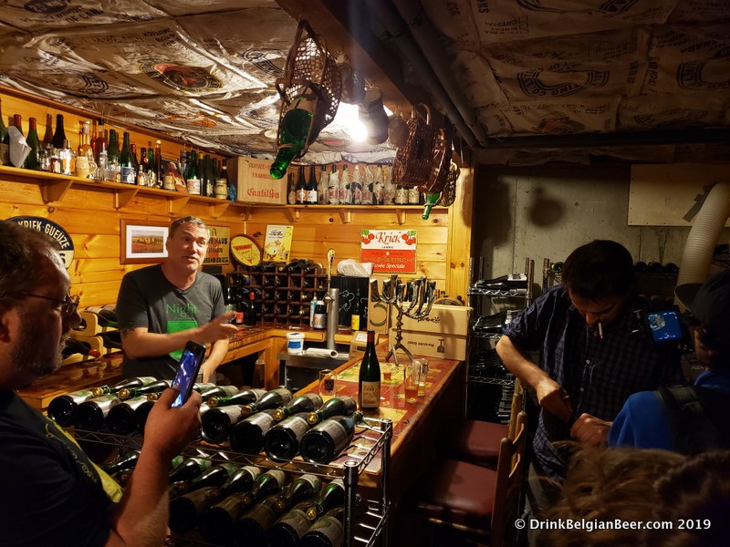 Christopher Lively (left) behind the bar in the lambic cellar at Ebenezer's Pub in Lovell, Maine. Raf Soef is on the right, opening a bottle with a corkscrew. 